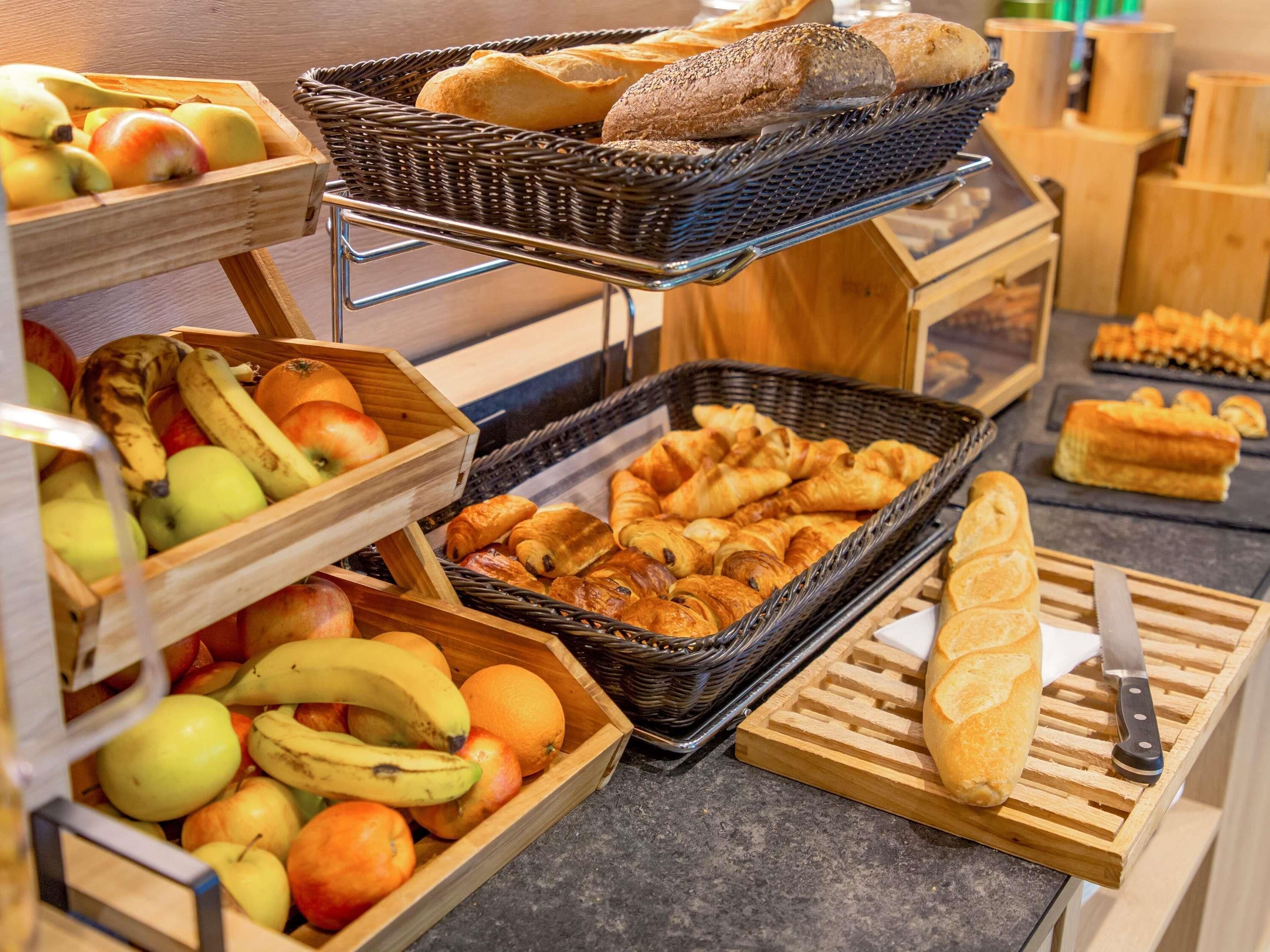A buffet setup with various food items including fruits, bread, and pastries.