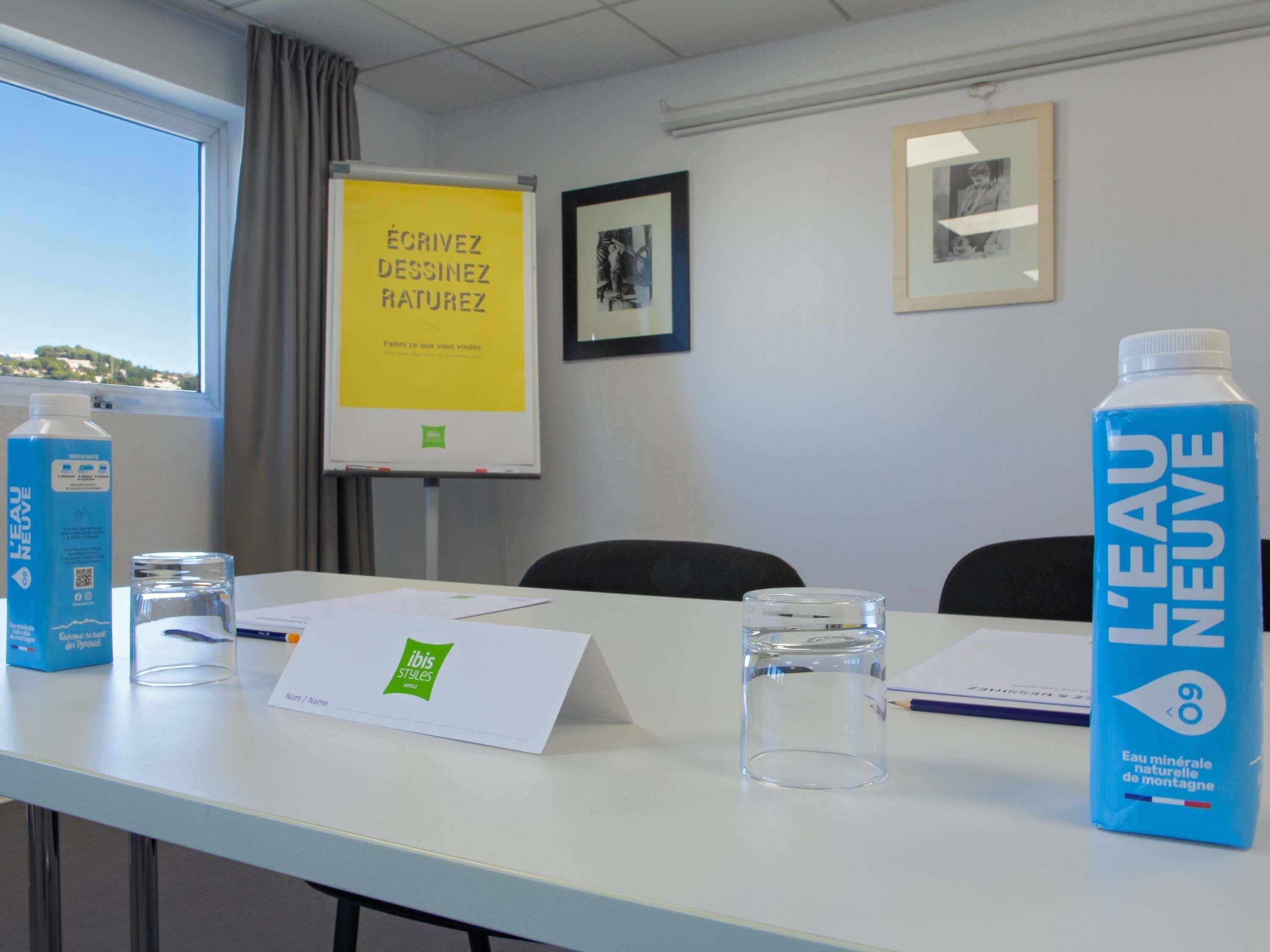 A conference room with a whiteboard, framed pictures, and water bottles on the table.