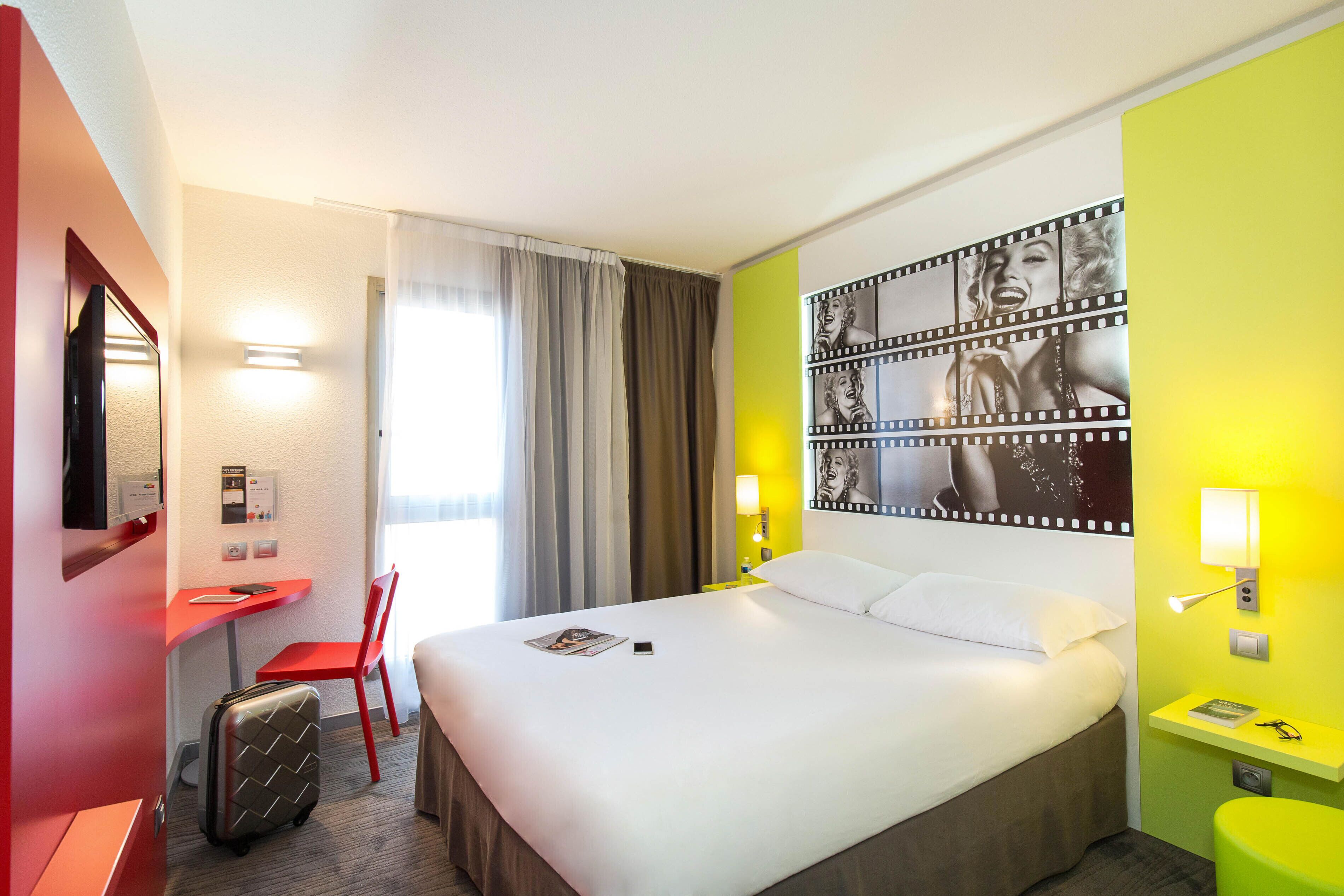 Ein Hotelzimmer mit Bett, Schreibtisch, Stuhl, Koffer und einem großen Wandbild.