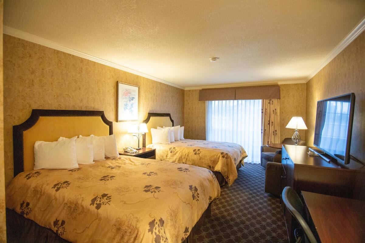 A hotel room with two beds, a desk, a chair, a television, and a window with curtains.