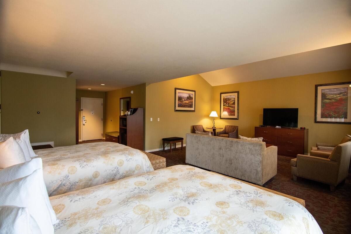 A hotel room with two beds, a sofa, a TV, and a desk.