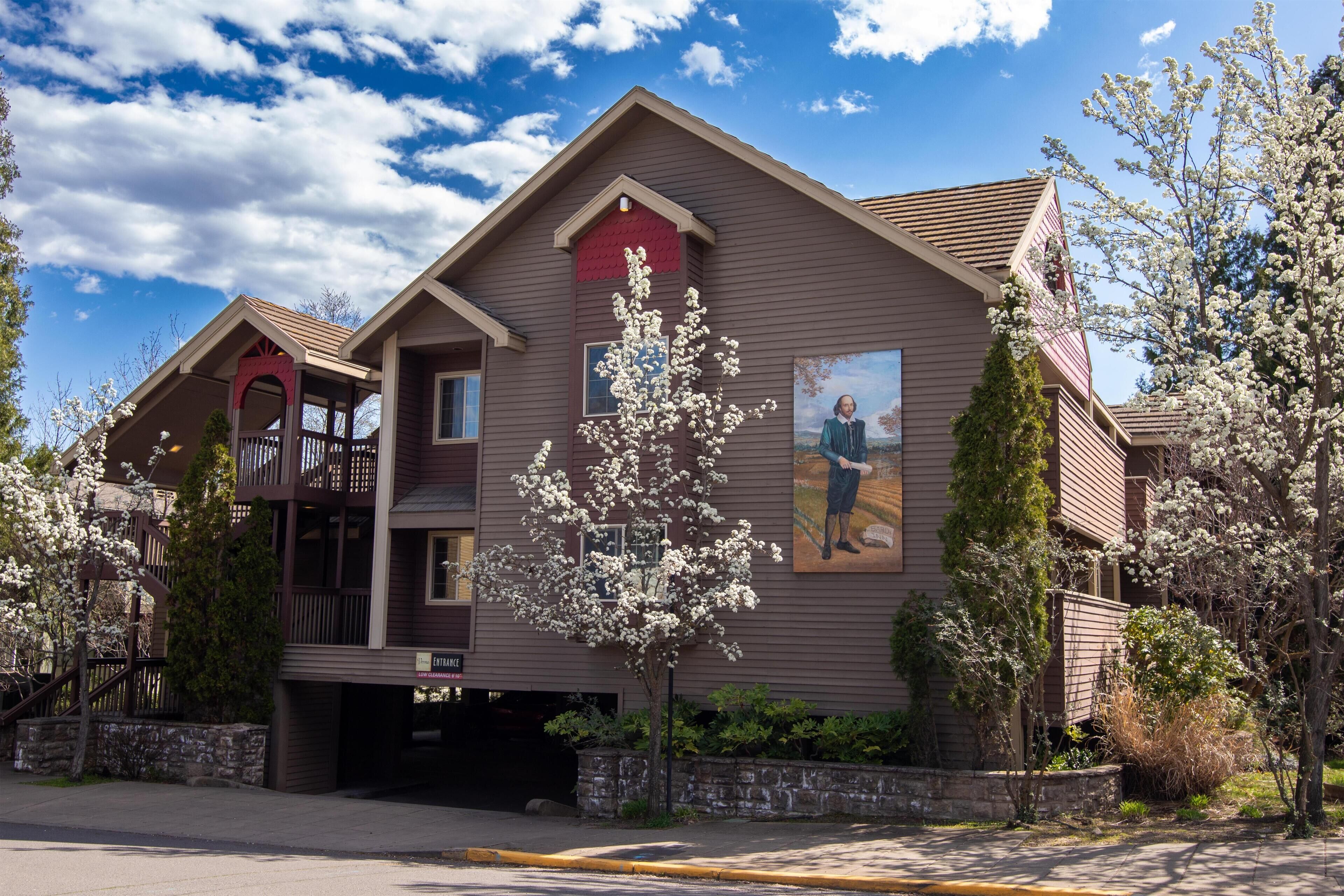 A two-story building with a balcony, a garage, and a landscaped area with trees.