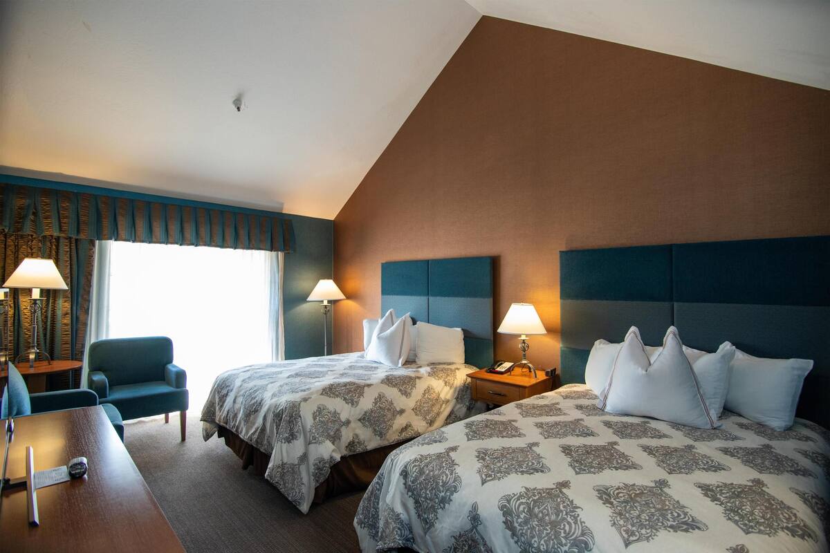 A hotel room with two beds, a desk, a chair, and lamps.