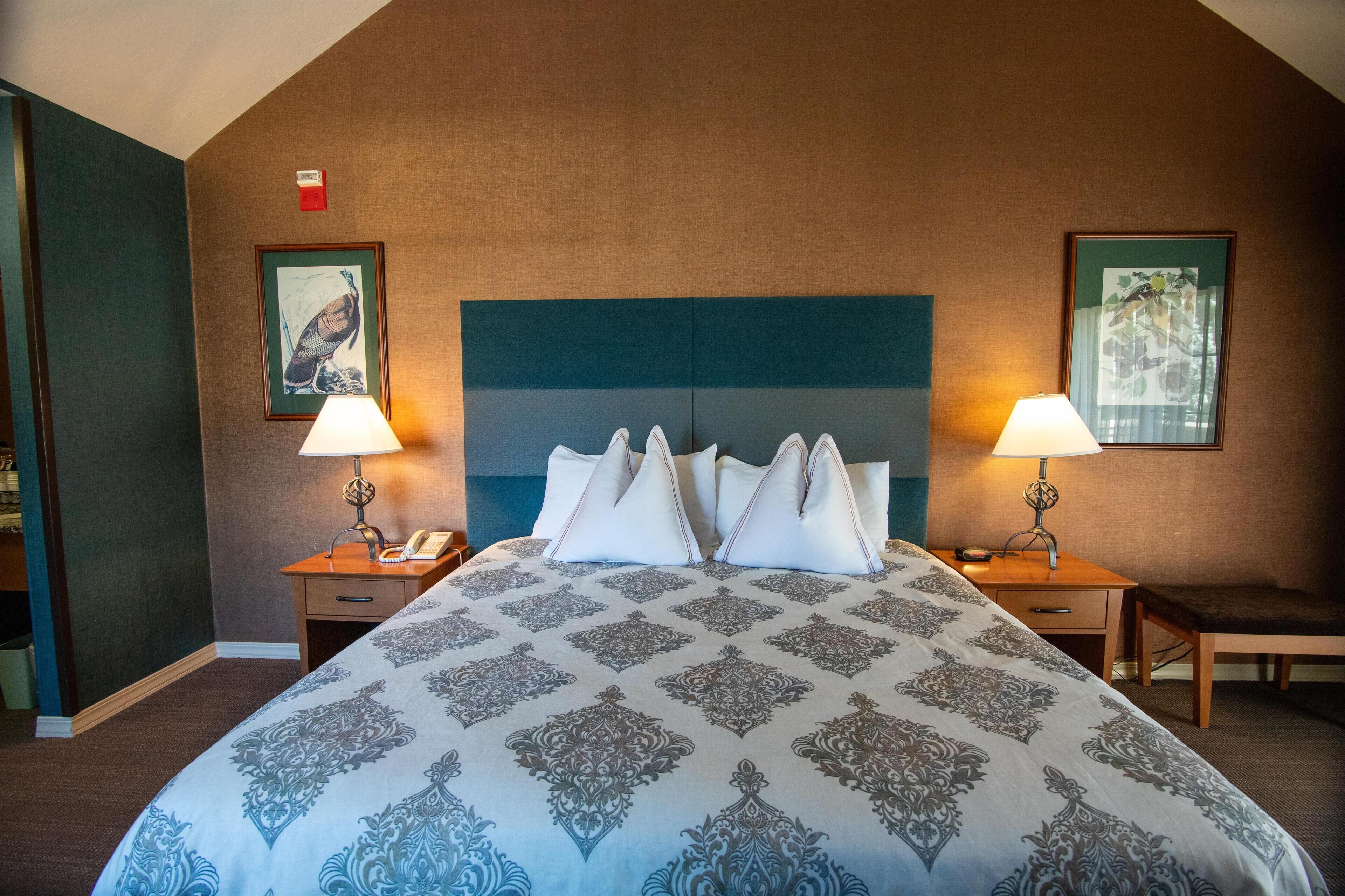 Une chambre d’hôtel avec un grand lit, deux tables de chevet avec des lampes, une tête de lit en bois et des œuvres d’art encadrées accrochées aux murs.