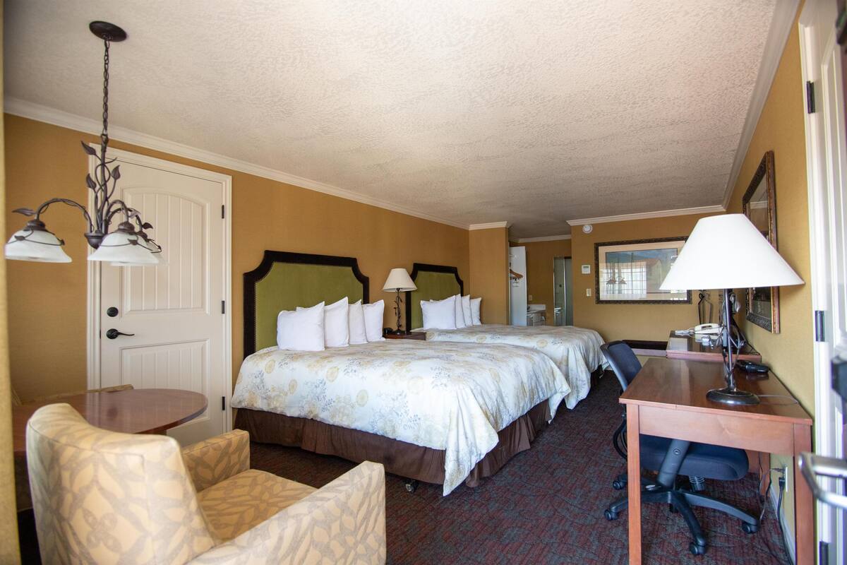 A hotel room with a large bed, a desk, a chair, and a lamp.