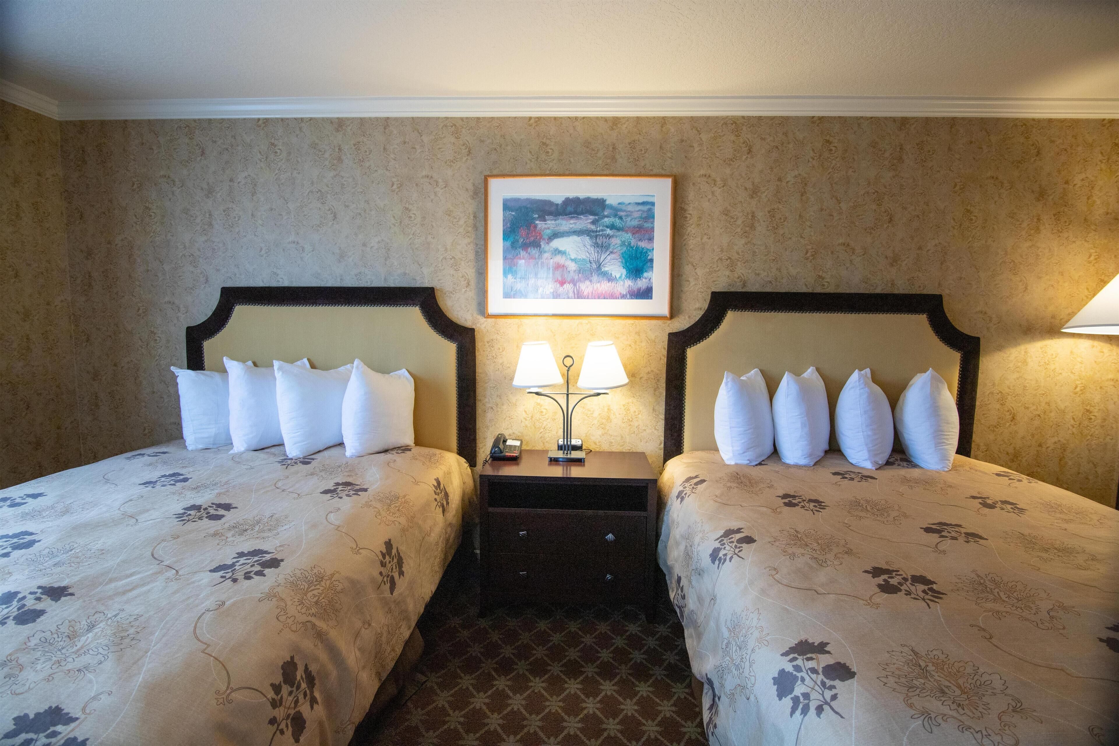 A hotel room with two beds, each with a headboard, a nightstand with a lamp, and a framed picture on the wall.