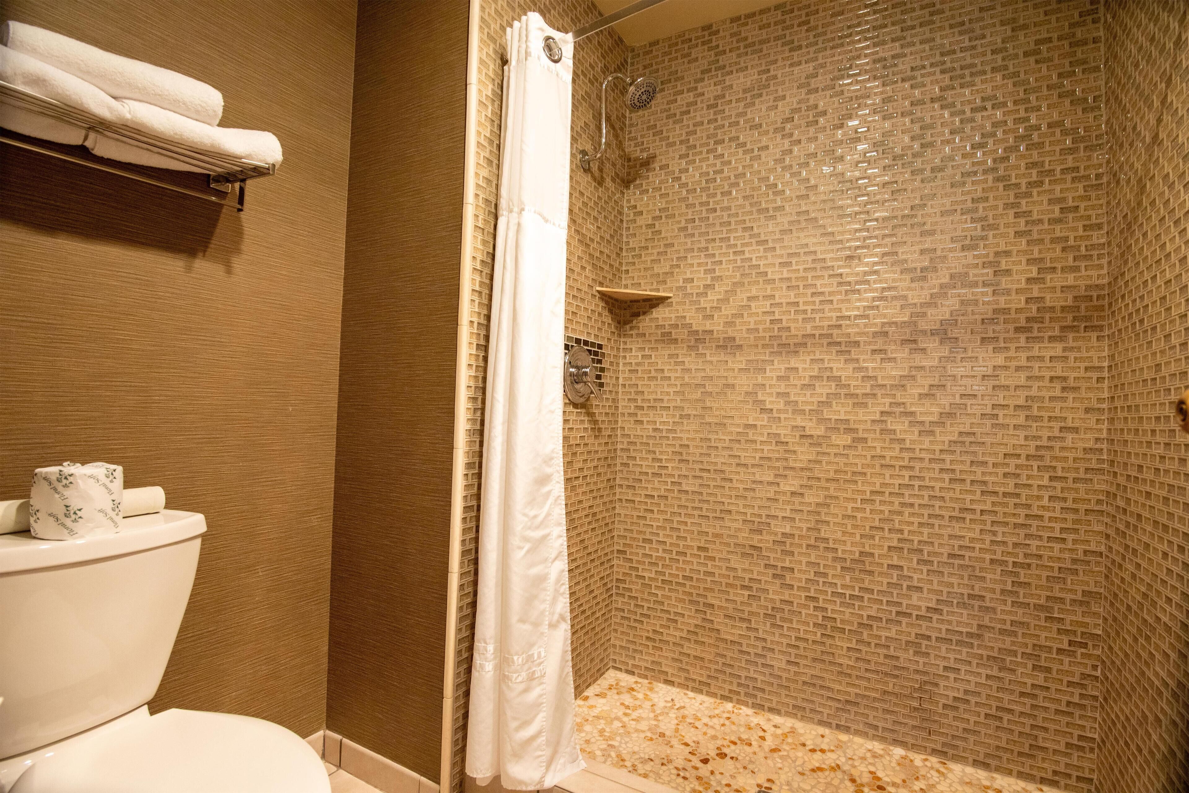 A bathroom with a toilet, a shower with a tiled wall, and a towel rack with towels.
