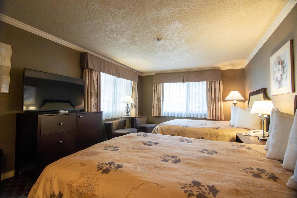 A hotel room with two beds, a TV, a desk, and a lamp.