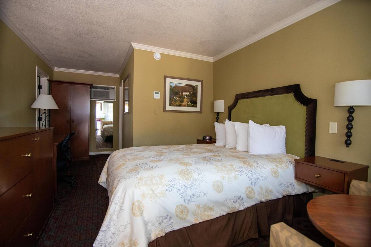 A hotel room with a large bed, a desk, a chair, a lamp, and a picture on the wall.