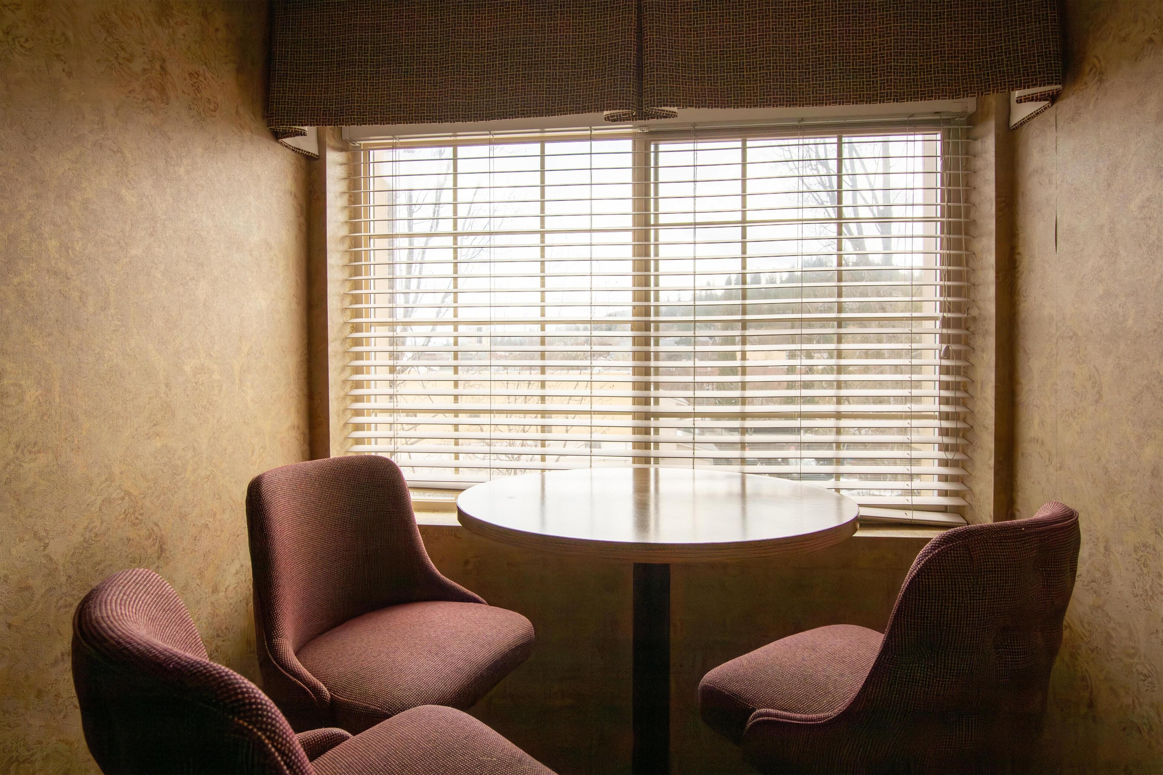 A room with a round table and two chairs, a window with blinds, and a textured wall.