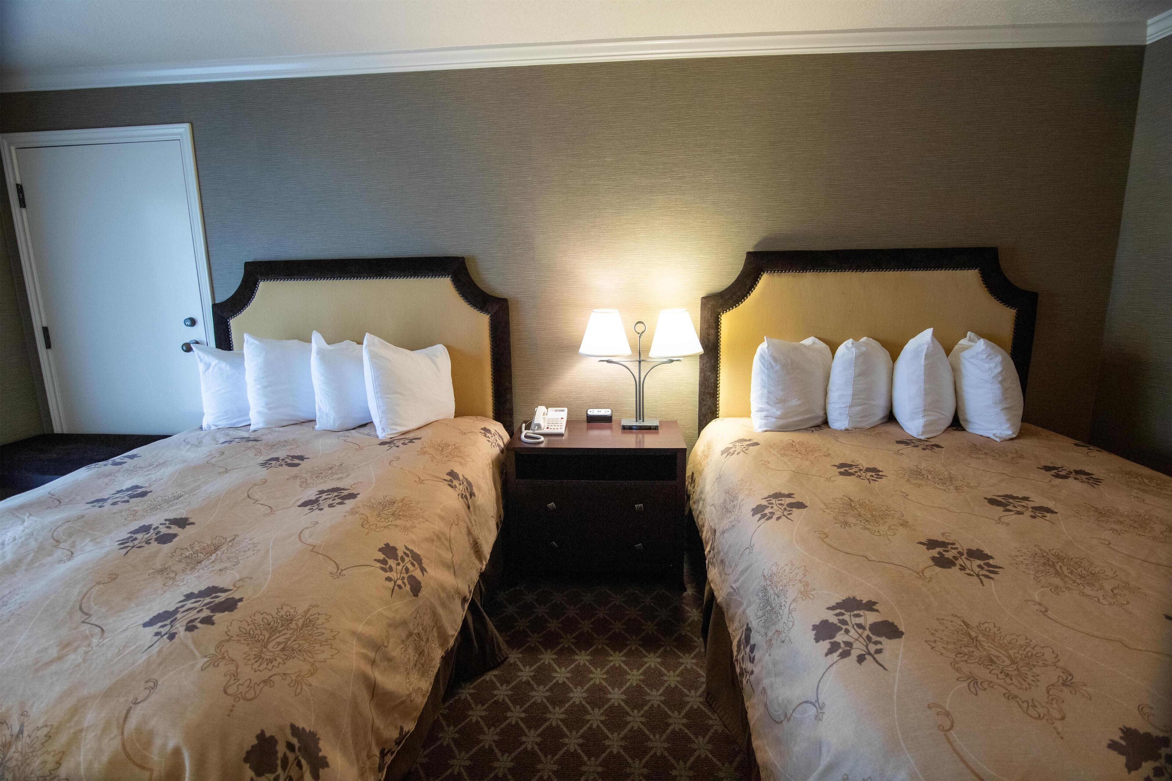 A hotel room with two beds, a nightstand with a lamp, and a door.