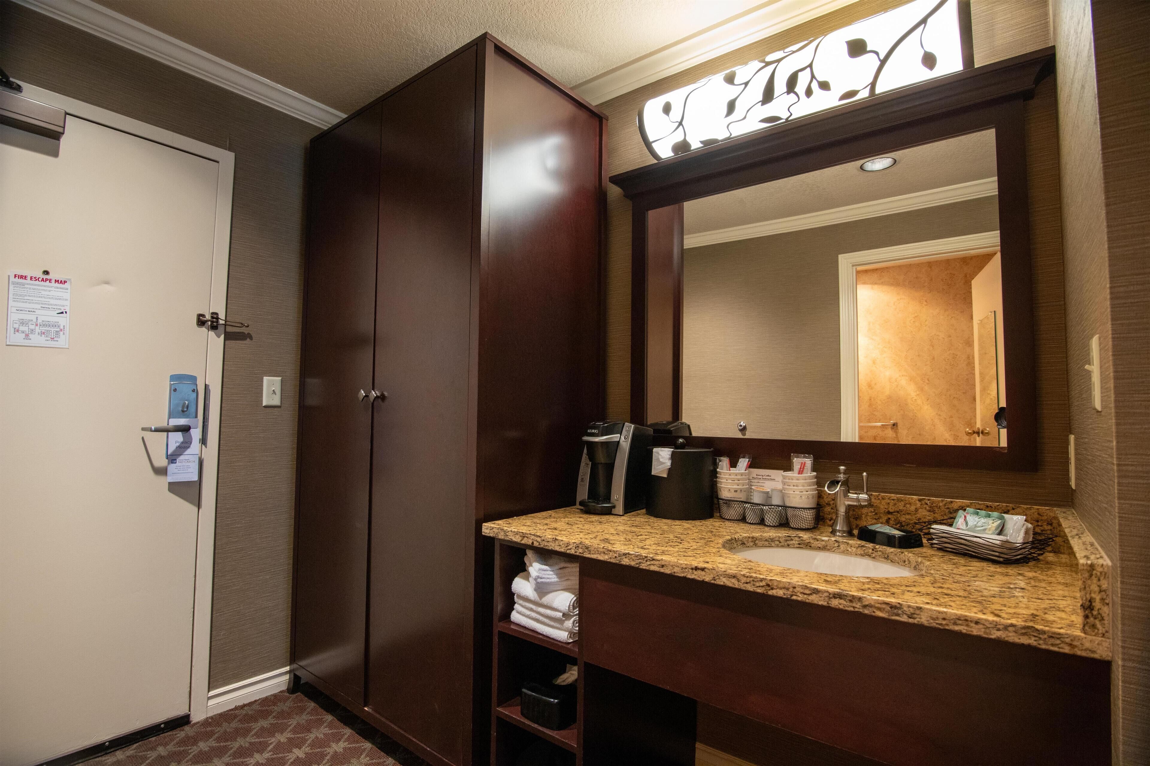 A hotel bathroom with a large mirror, a sink, and a cabinet.