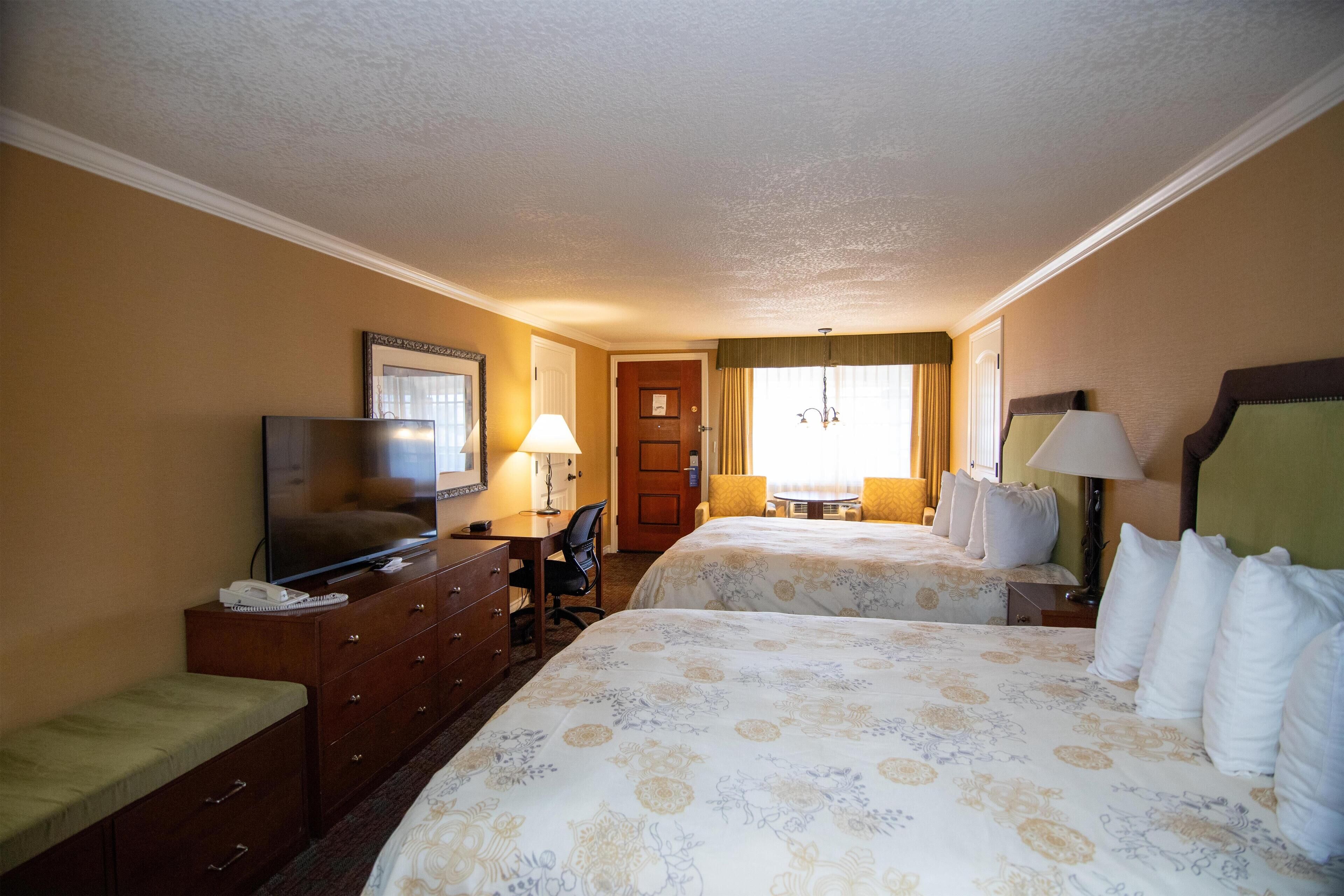 A hotel room with two beds, a television, a desk, and a chair.