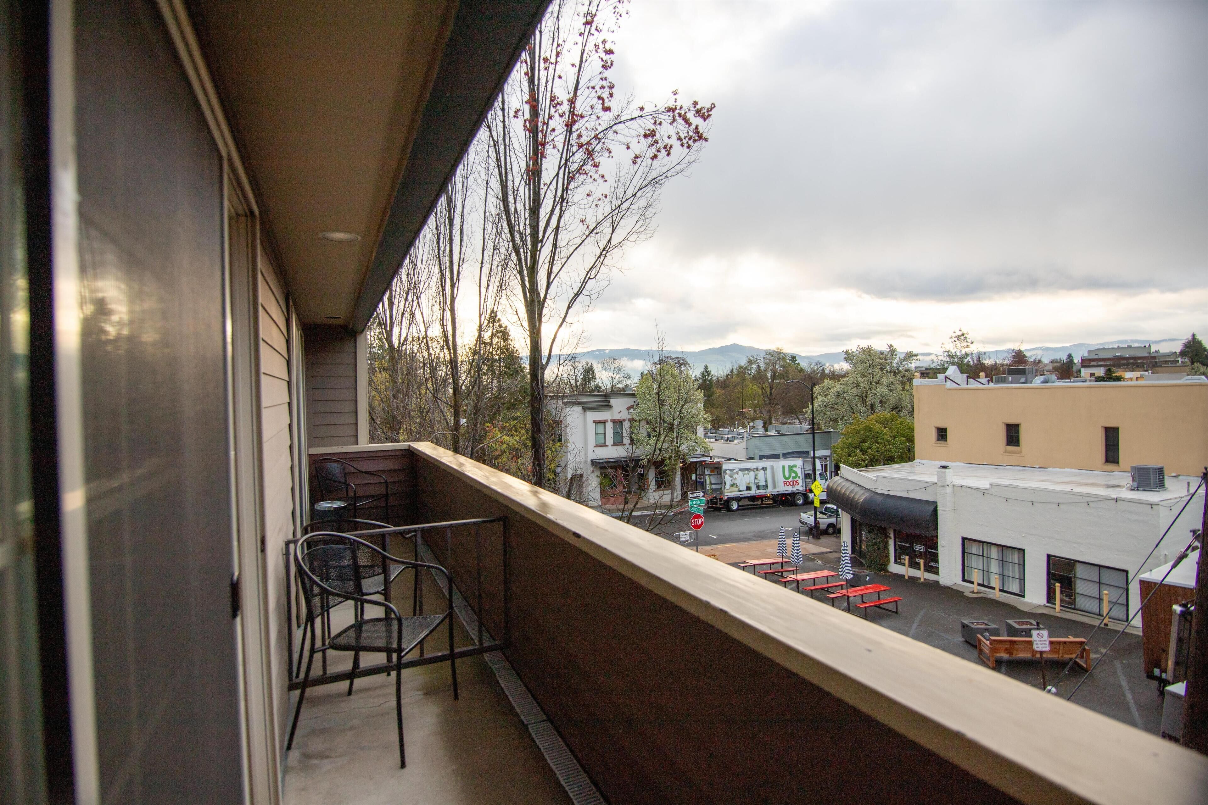 A balcony with a view of a parking lot and buildings, including a food truck.