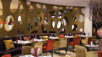 En moderne restaurant med et unikt vægdesign bestående af runde udskæringer, komfortable siddepladser og en stor potteplante.