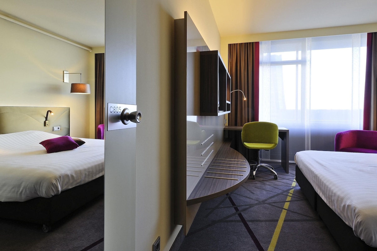 Habitación de hotel con dos camas, un escritorio, una silla, un televisor y una ventana con cortinas.