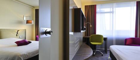 Ein Hotelzimmer mit zwei Betten, einem Schreibtisch, einem Sessel, einem Fernseher und einem Fenster mit Vorhängen.