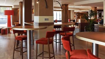 Rebedor modern d'hotel amb taules rodones i cadires vermelles, un gran pilar i vista al carrer.