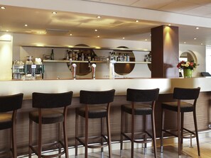 A bar area with stools, a bar counter, and a selection of bottles and glasses.