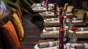 A restaurant with tables set for dining, featuring red candle-like centerpieces and neatly folded napkins.