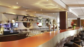 A modern bar area with a curved counter, multiple seating options, and a variety of bottles and glasses on shelves.
