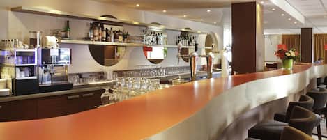 Zona de bar moderna con un mostrador curvo, diversas opciones de asientos y una variedad de botellas y copas en estanterías.