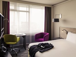 Una habitación de hotel con cama, escritorio, silla y lámpara.