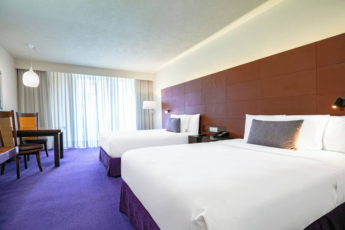 A hotel room with two beds, a desk, and a chair.