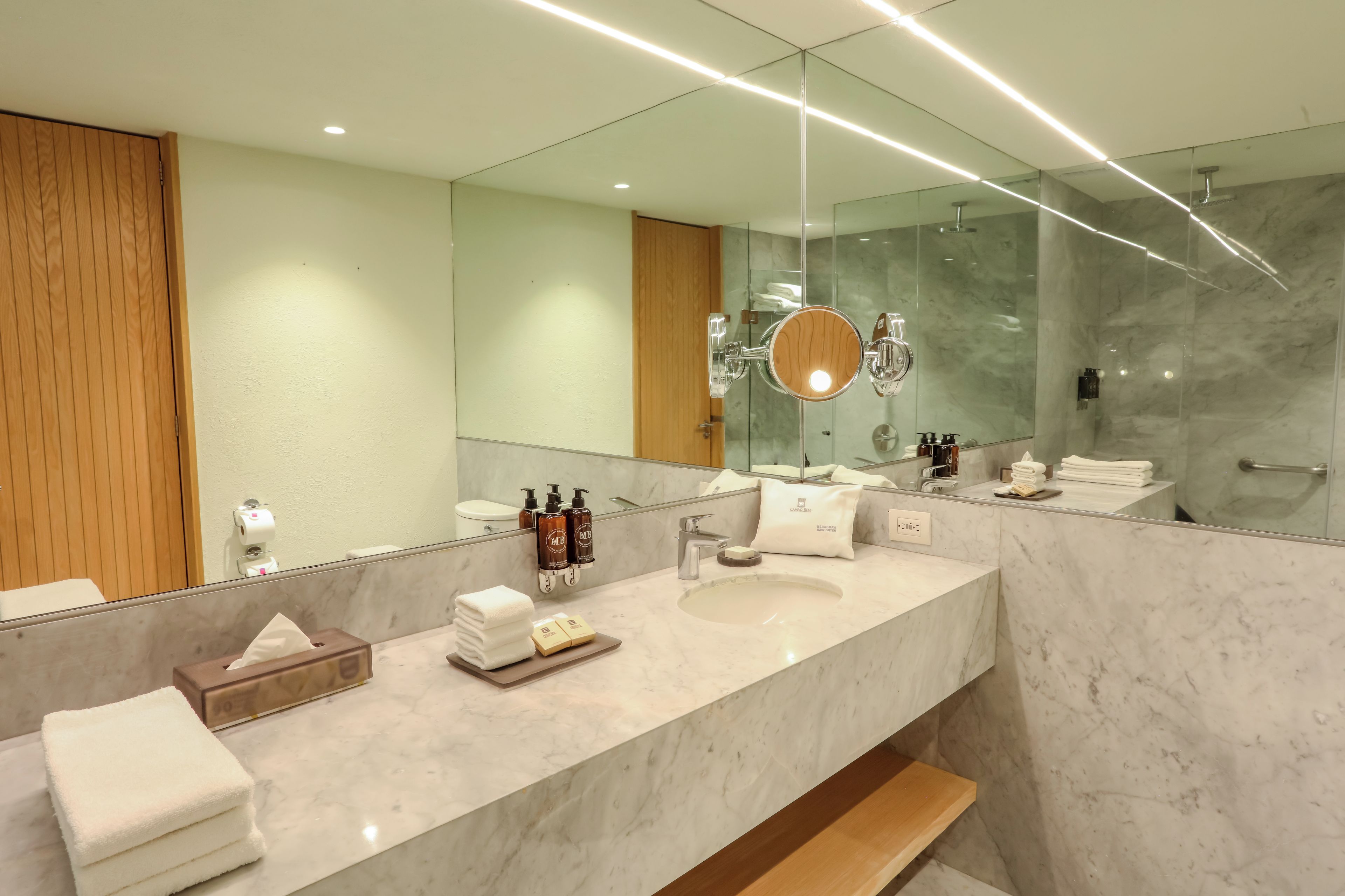 Un baño moderno con un espejo grande, encimeras de mármol y cabina de ducha de vidrio.
