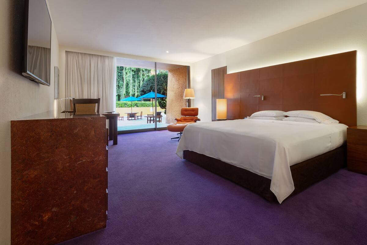 A hotel room with a large bed, a desk, a chair, and a view of the outdoors.