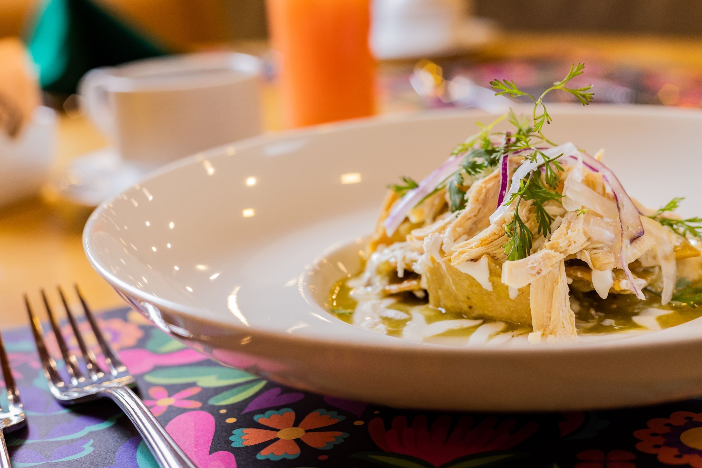 A plate of food with a fork and a cup on a table with a colorful tablecloth.
