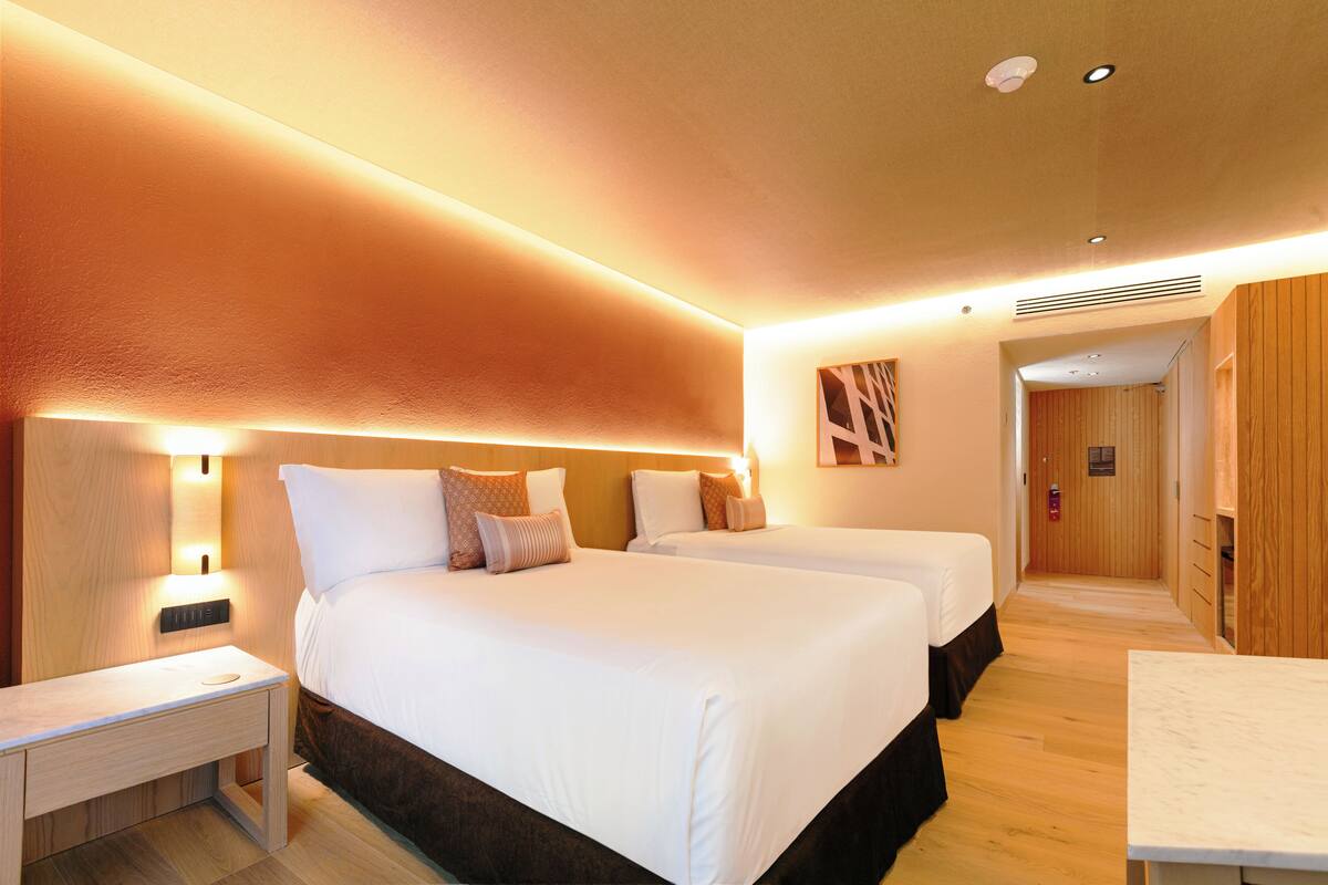 A hotel room with two beds, a nightstand, a desk, and a wooden wall panel.