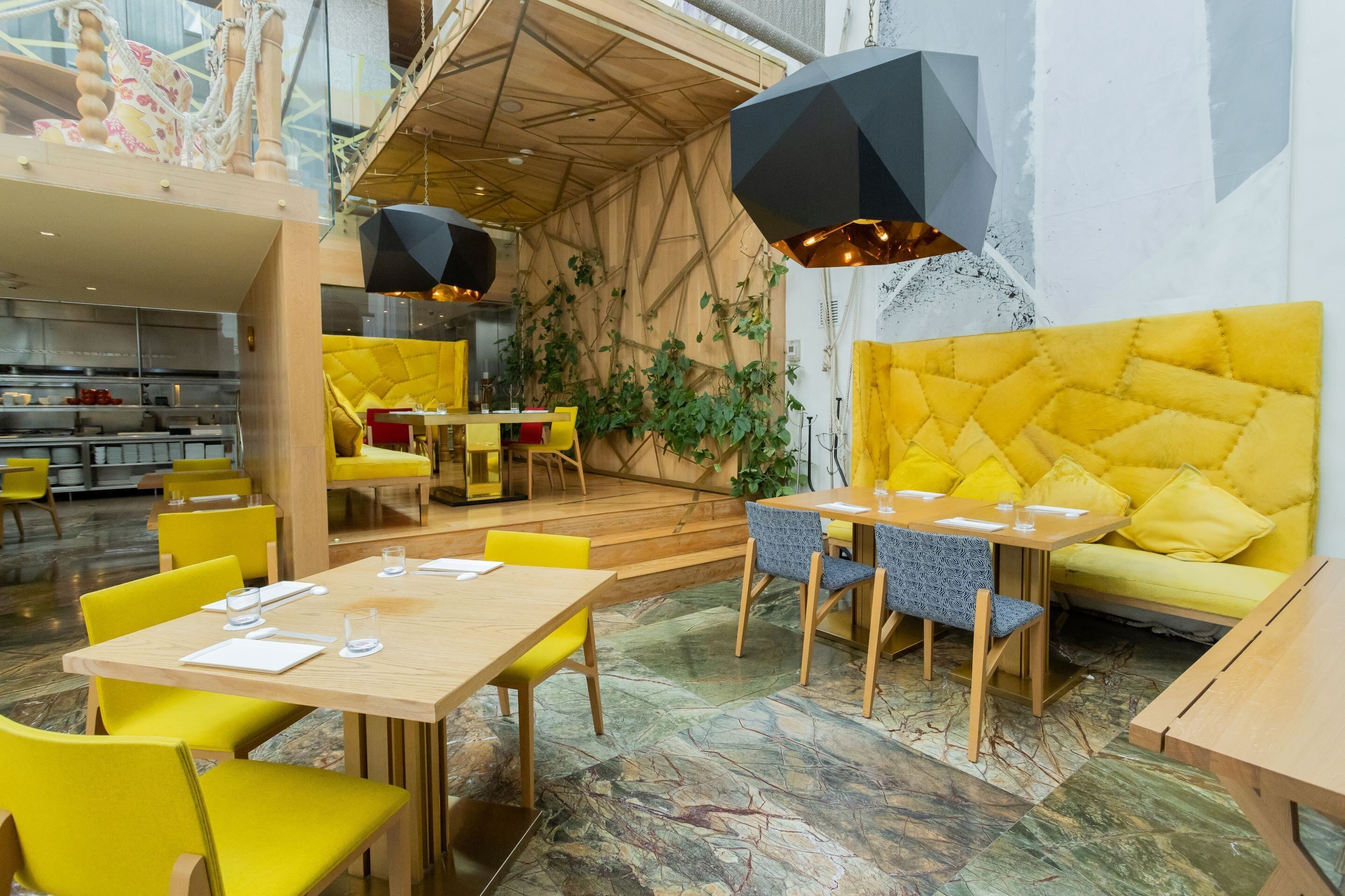 A modern restaurant with yellow chairs and tables, a wooden ceiling, and a yellow sofa.