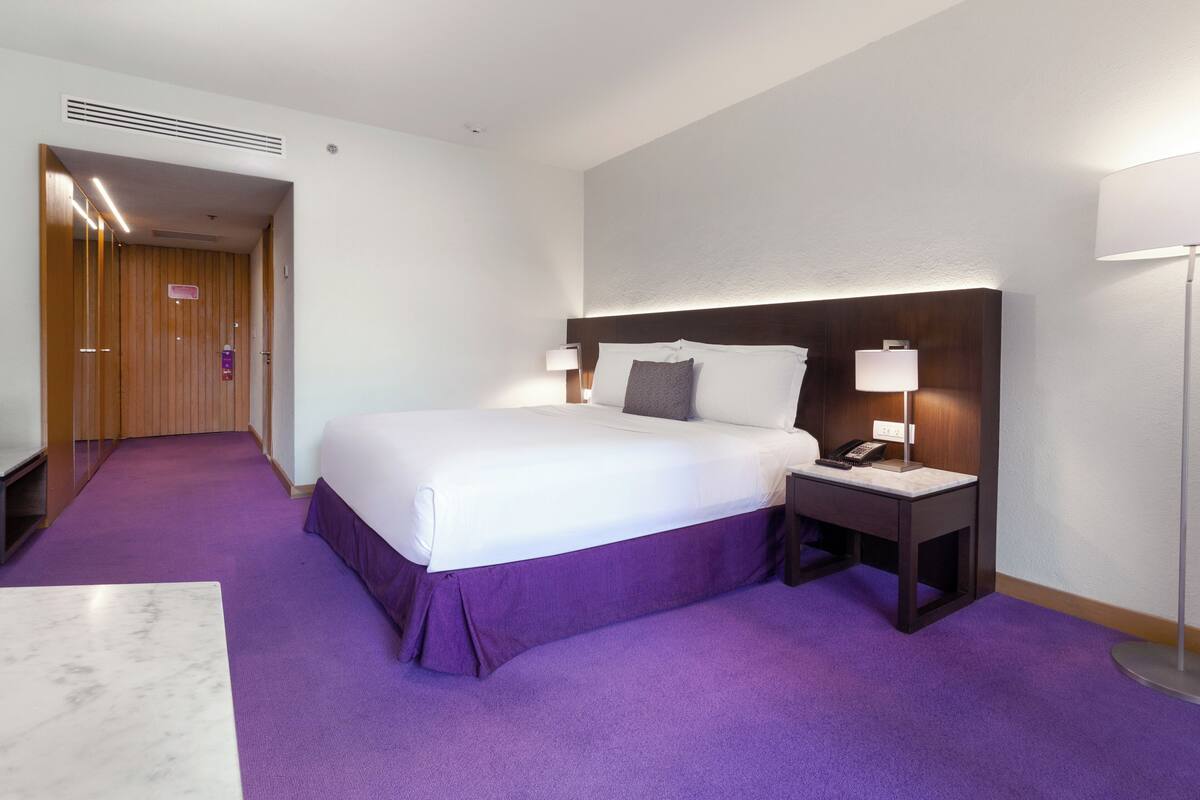 A hotel room with a large bed, a bedside table with a lamp, a phone, and a headboard.