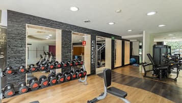 Un gimnasio con equipo de levantamiento de pesas, un espejo y una pared de piedra.