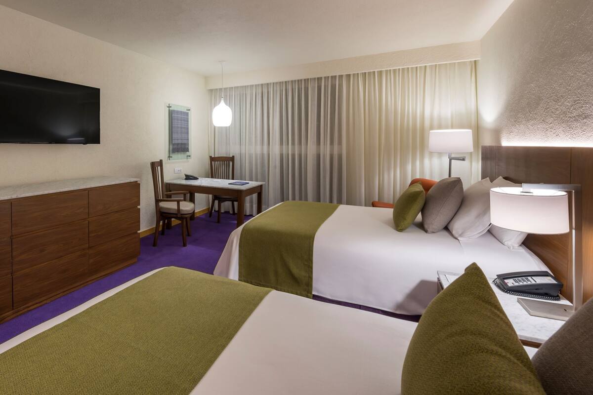 A hotel room with two beds, a desk, a TV, and a minibar.