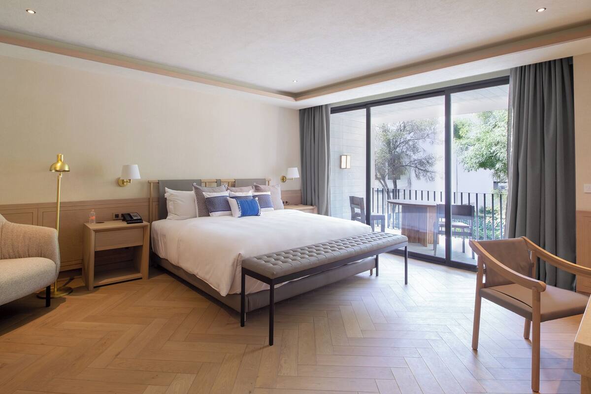 A hotel room with a large bed, a desk, a chair, and a view of the outdoors.