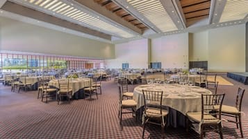 Une salle de banquet spacieuse, dotée de nombreuses tables rondes dressées pour le repas, avec un tapis à motifs et un design de plafond moderne.