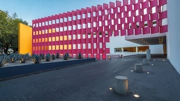 Um edifício moderno com fachada rosa, um pátio central e uma estrutura amarela à esquerda.
