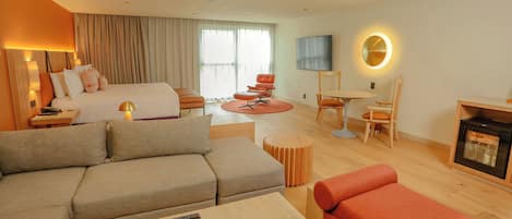 Habitación de hotel con cama, sofá, mesa de centro, televisor, chimenea y zona de comedor con sillas y mesa.