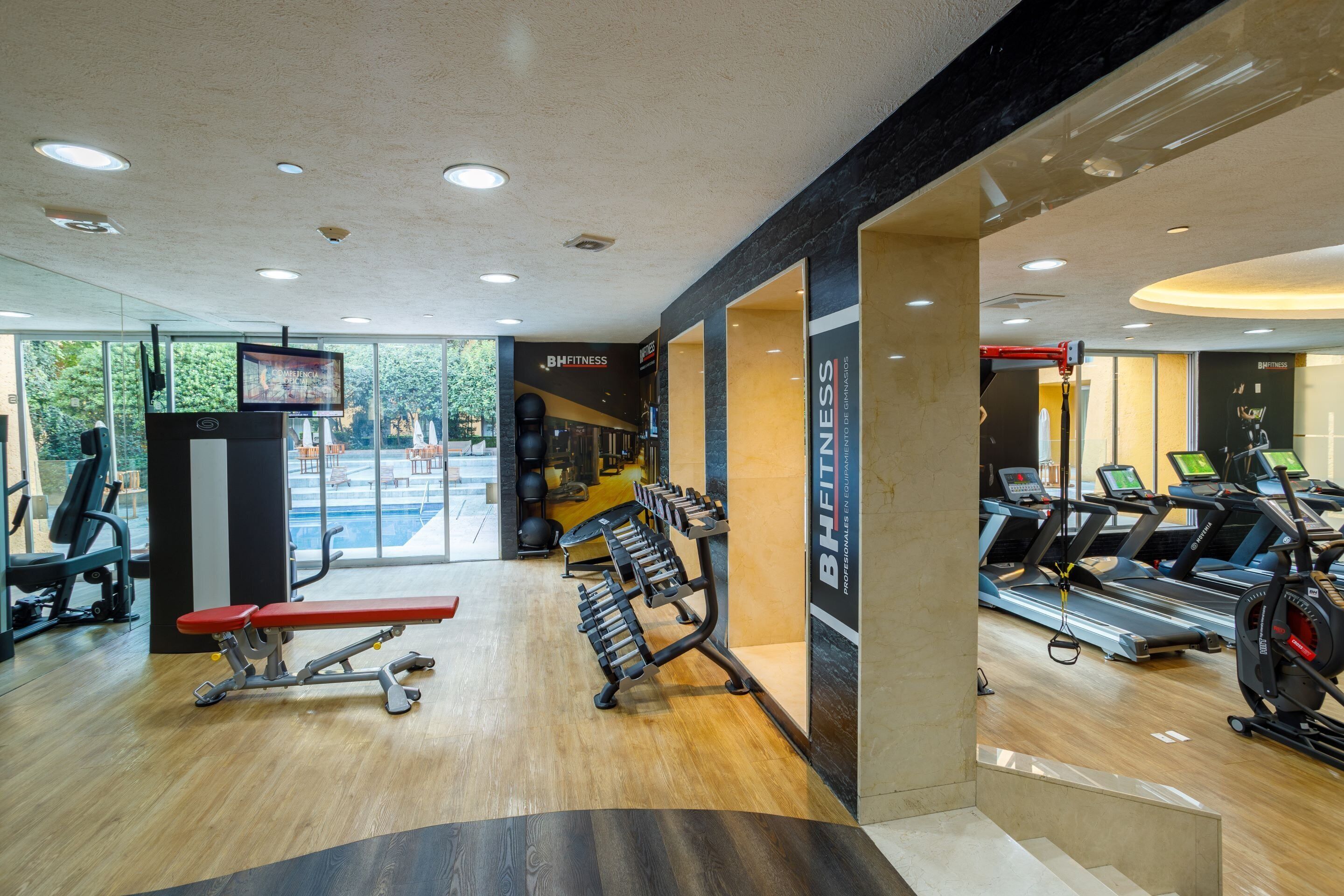 Un gimnasio con cintas de correr, bancos de pesas y pelotas de ejercicio.