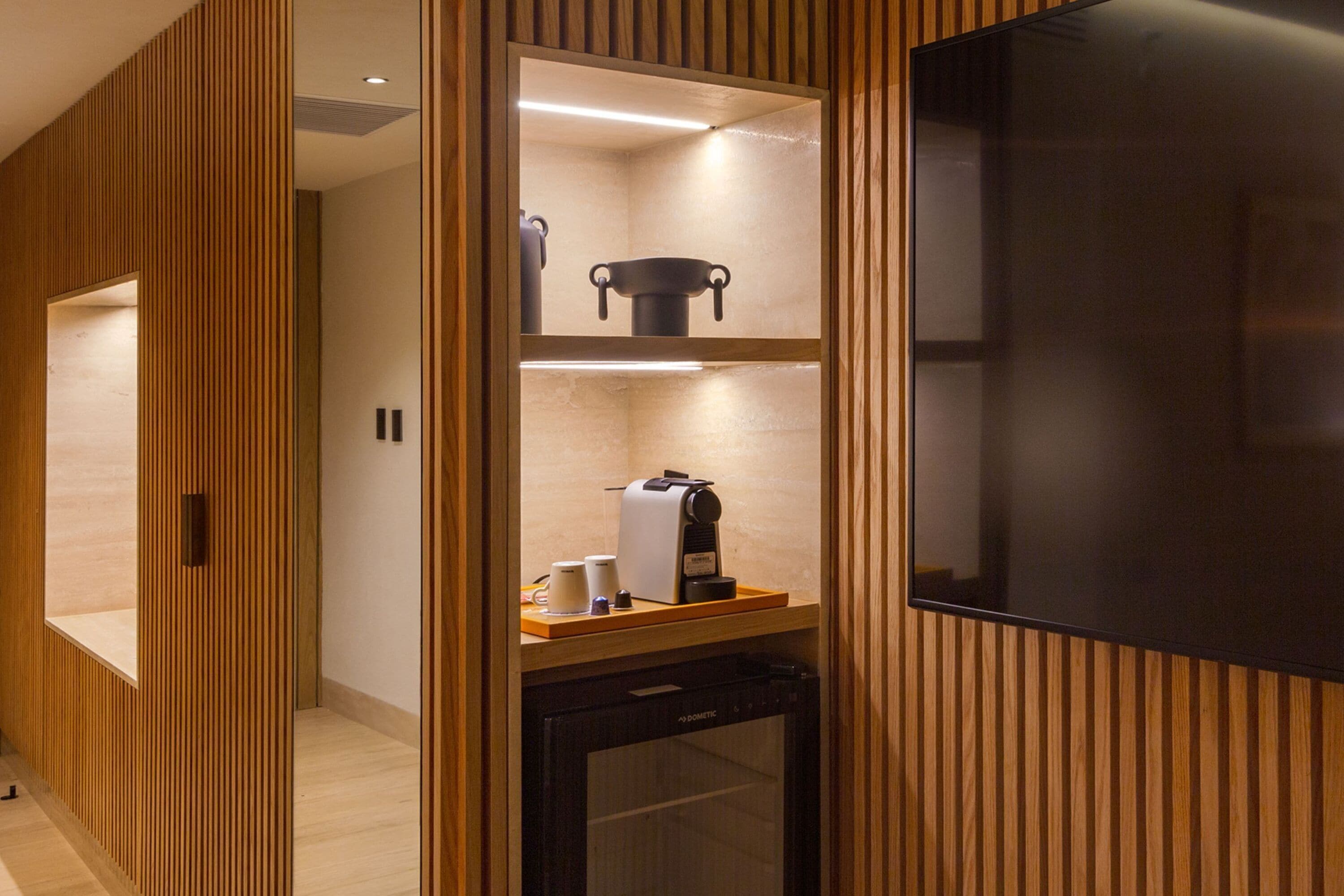 A modern bathroom with wooden paneling, a built-in coffee maker, and a large mirror.