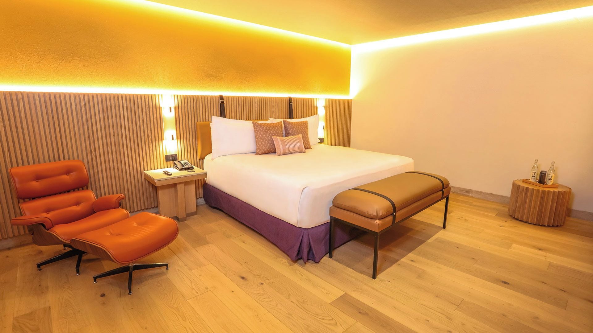 Een hotelkamer met een bed, een stoel, een nachtkastje met een lamp en een klein houten bijzettafeltje.