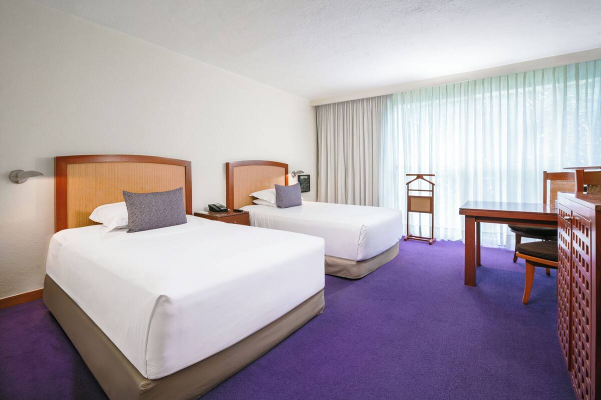 A hotel room with two beds, a desk, and a chair.