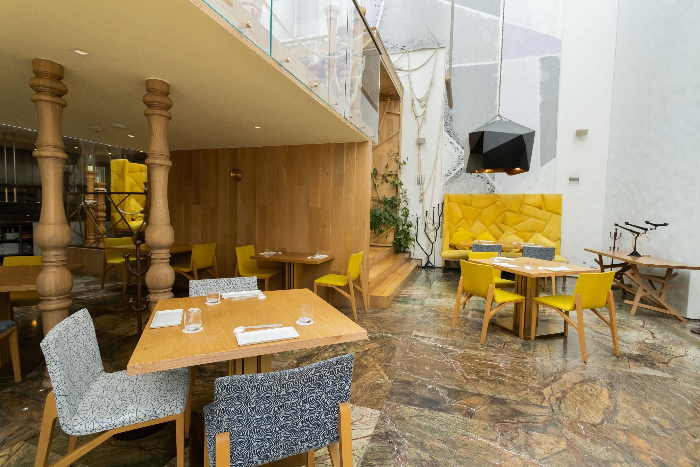Un comedor moderno con mesas y sillas de madera, un techo alto y un piso de mármol.