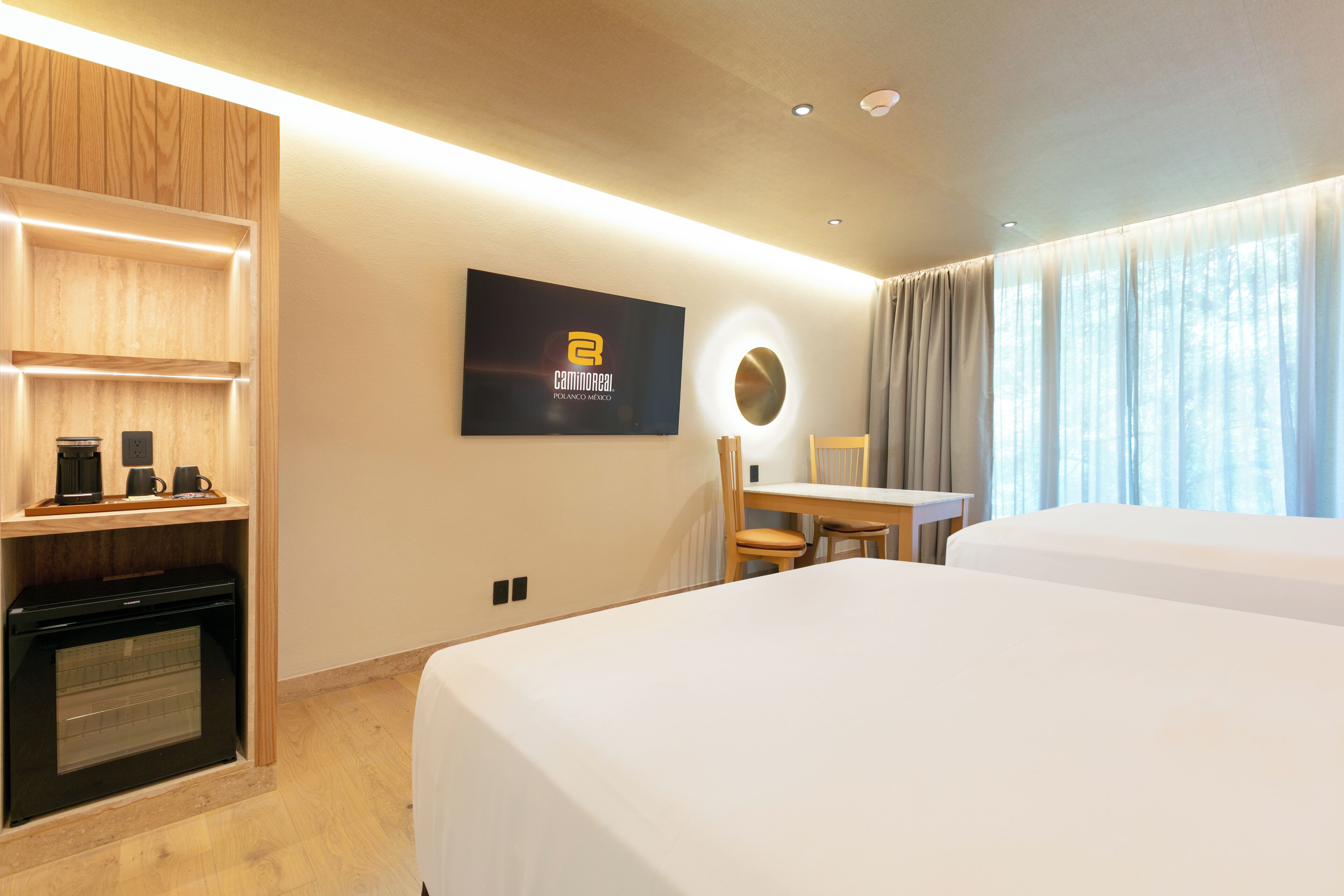 Une chambre d’hôtel équipée d’un lit, d’un bureau, d’une chaise, d’un téléviseur fixé au mur et d’un mini-bar.