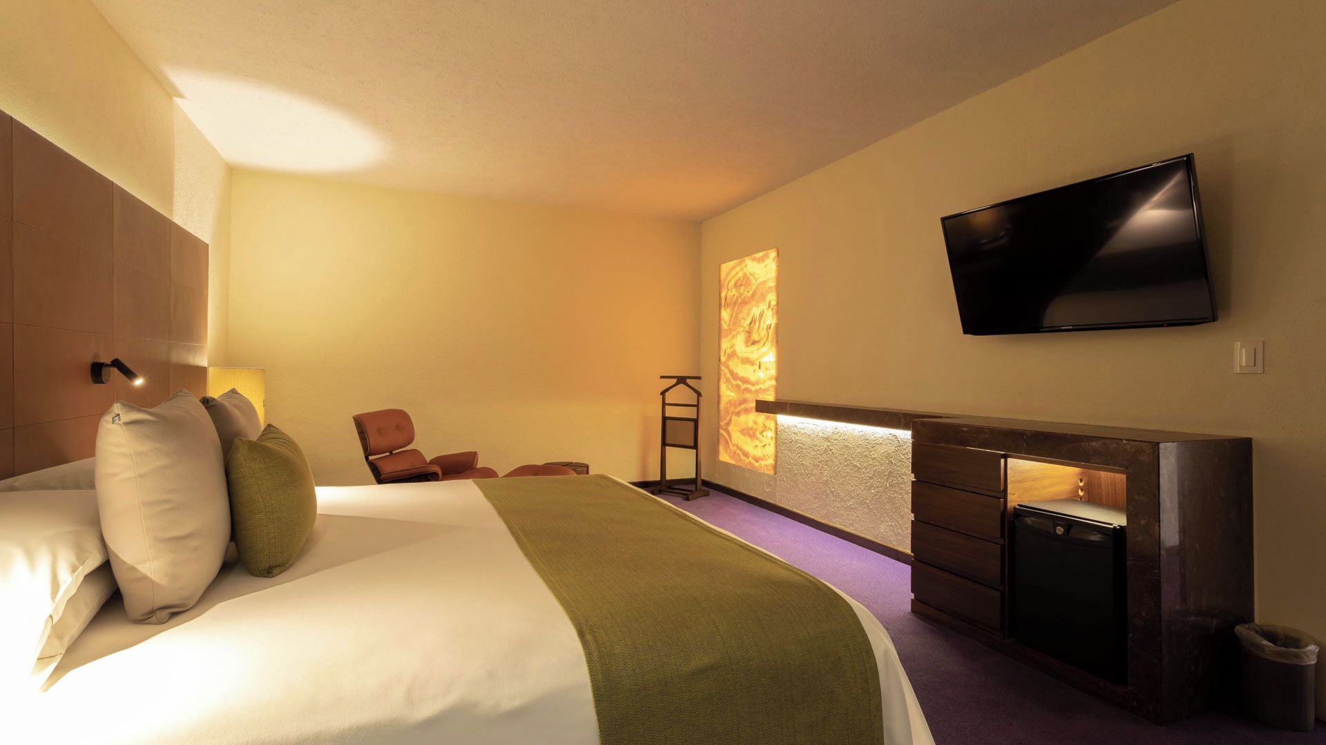 A hotel room with a bed, a television mounted on the wall, a fireplace, and a seating area with chairs.