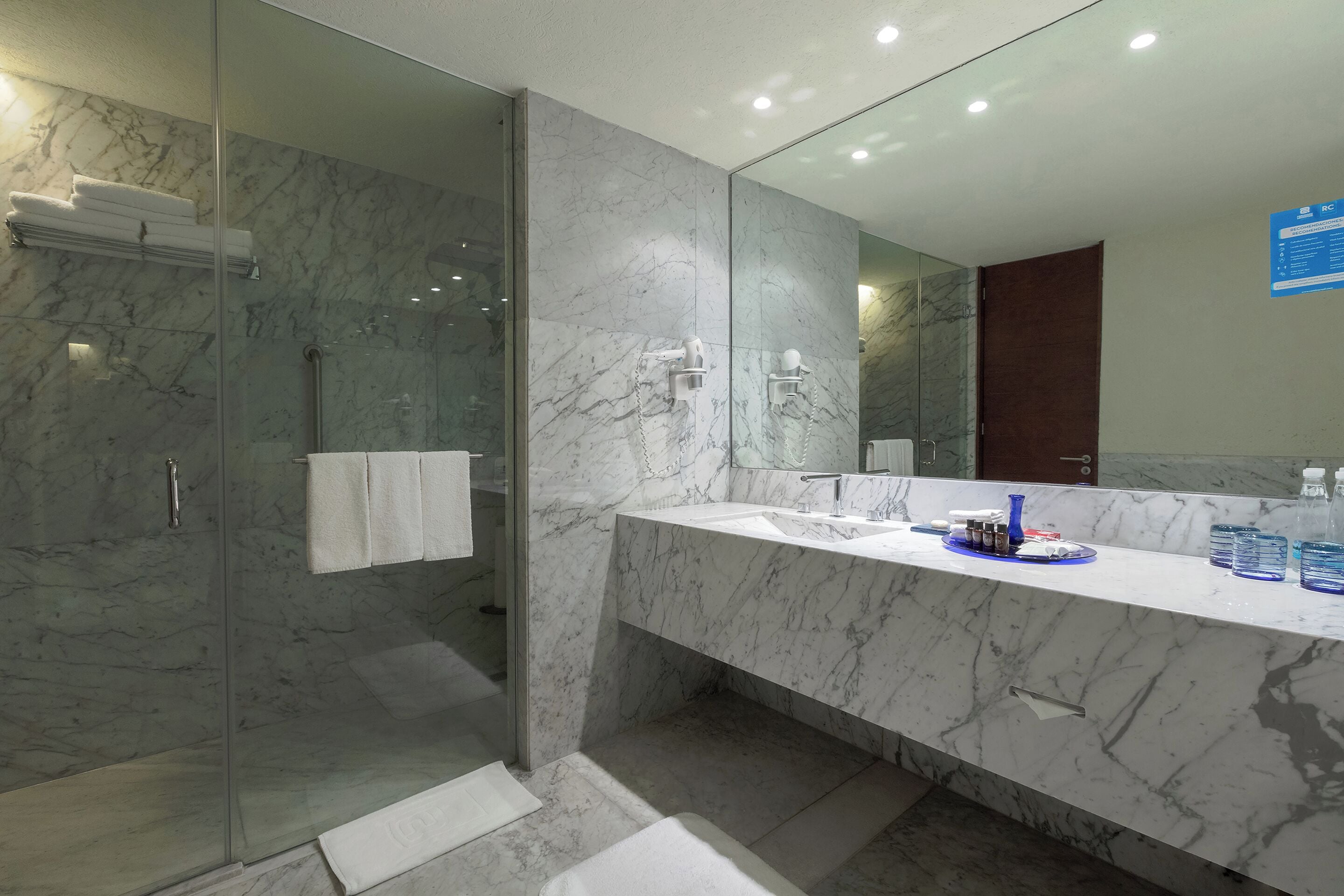 Une salle de bain moderne dotée d’une douche à parois de verre, d’un comptoir en marbre et d’un grand miroir.