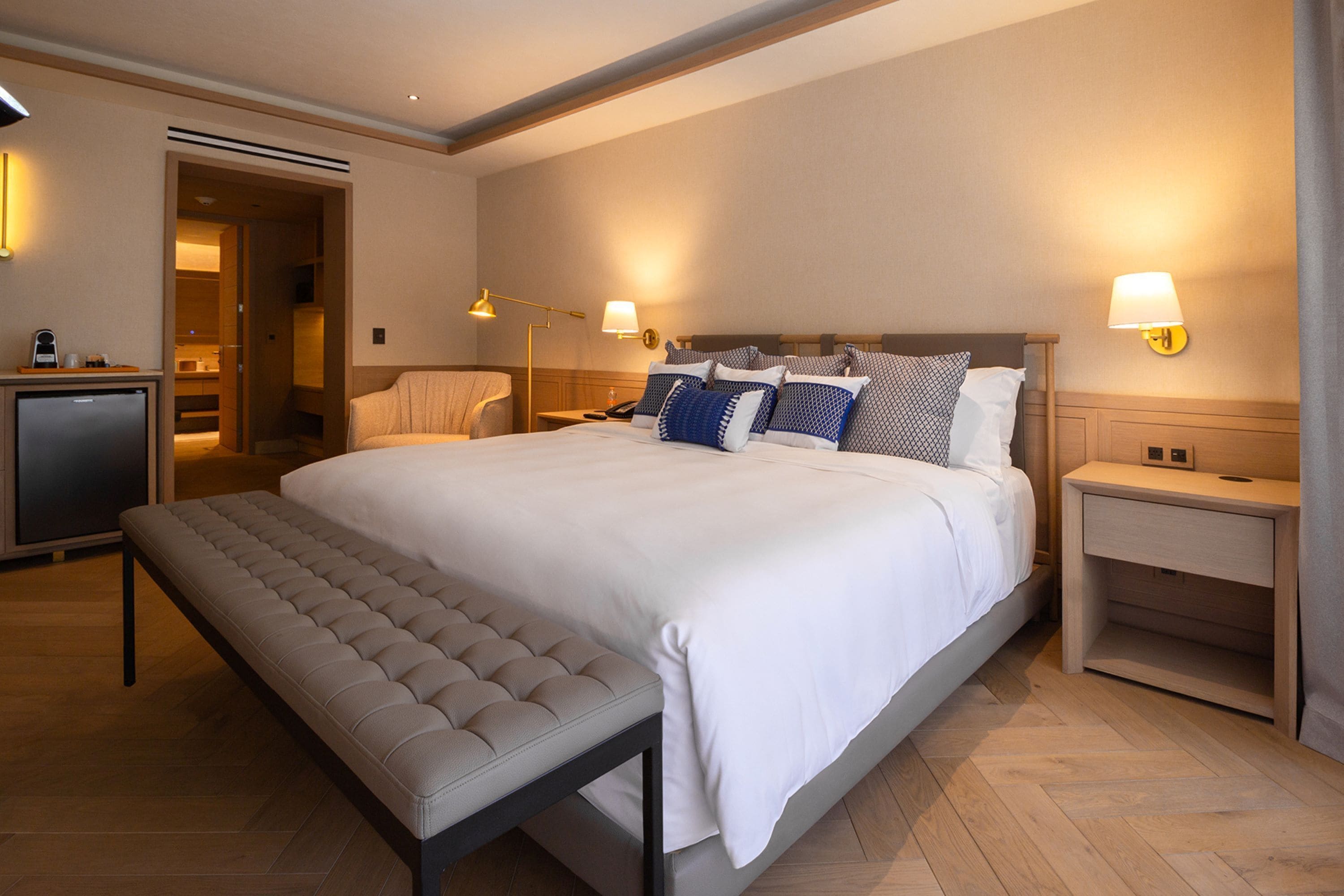 Una habitación de hotel moderna con una cama grande, mesitas de noche, un banco y un escritorio con una lámpara.