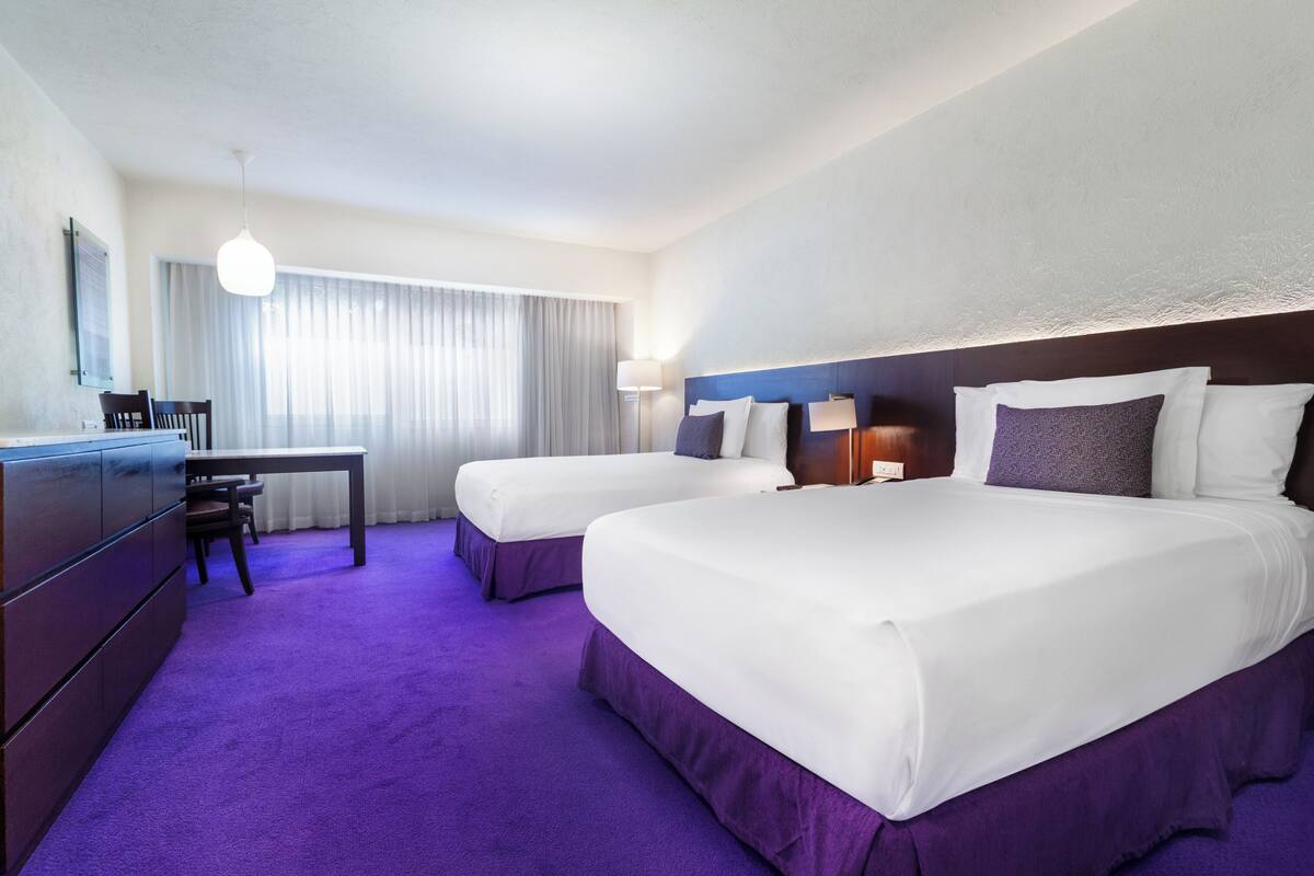 A hotel room with two beds, a desk, and a chair.
